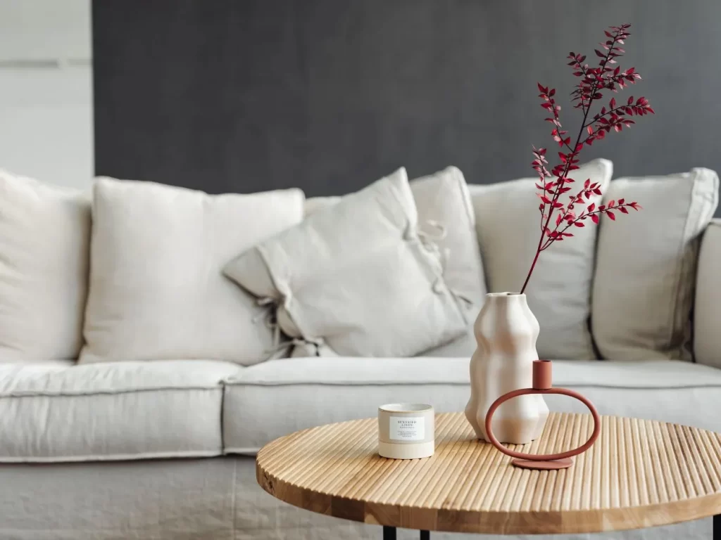 Scorcio di divano bianco con cuscini, con tavolino di legno con sopra vaso e candela profumata